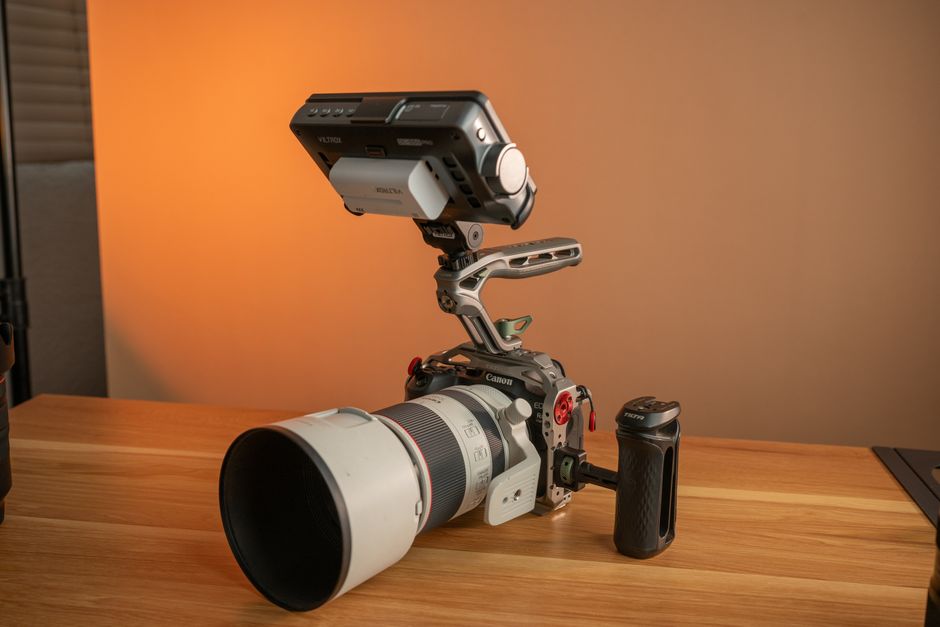 Detailed view of a professional camera with telephoto lens and monitor setup on a wooden surface.